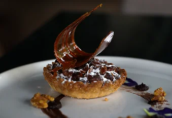 Élégante tarte gourmande décorée de caramel et servie sur une assiette de haute cuisine.